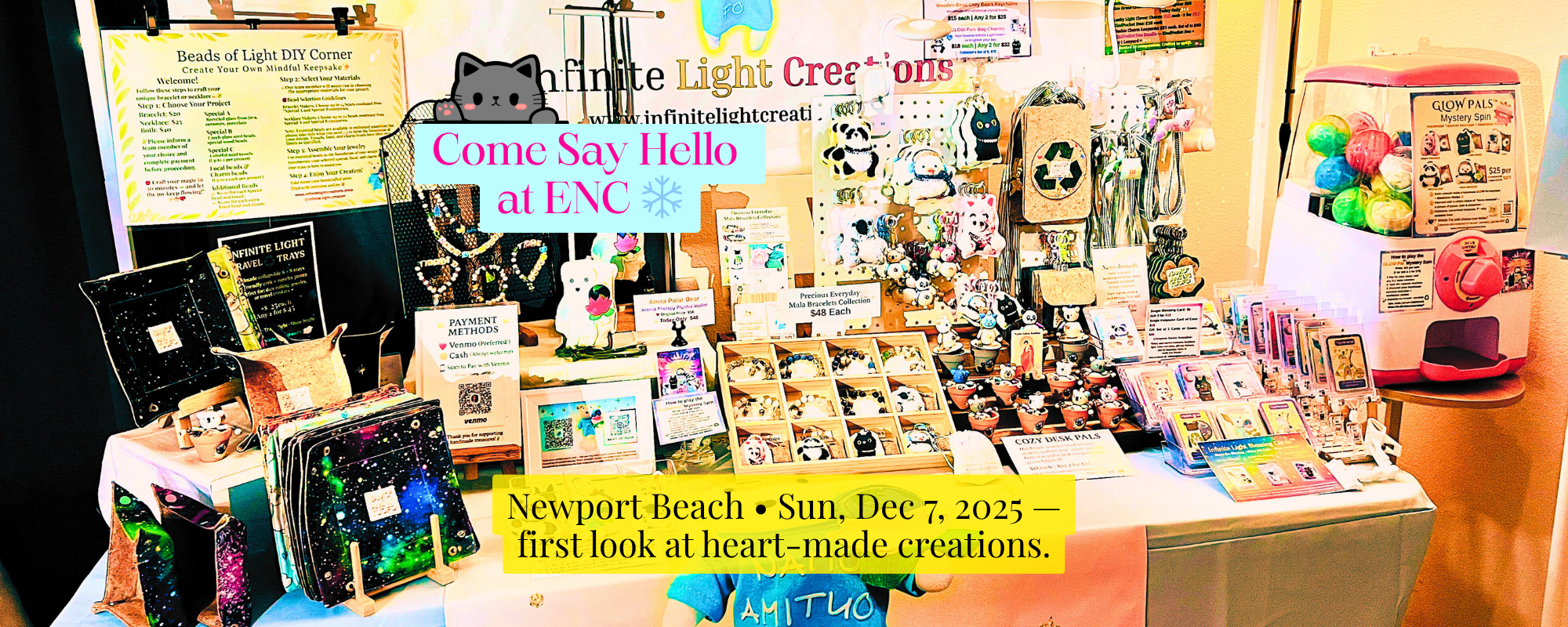 Infinite Light Creations pop-up booth with travel trays, Glow Pals, malas, and gashapon machine at artisan market.